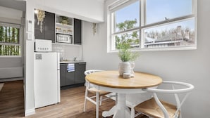 Une cuisine moderne avec des meubles blancs, un four à micro-ondes et un réfrigérateur. On y trouve une table à manger avec des chaises blanches et un vase avec une plante.
