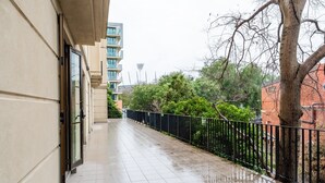 A wet corridor with a tiled floor, a black metal fence, and a tree on the right. - Chic 1-Bed in East Melbourne with Gym & Pool (East Melbourne)