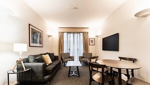 A hotel room with a sofa, two armchairs, a small table, a dining table with chairs, a flat-screen TV, and a large window with curtains. - Chic 1-Bed in East Melbourne with Gym & Pool (East Melbourne)