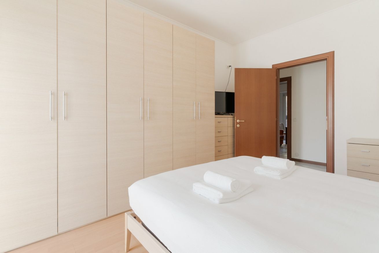 Een slaapkamer met een bed, een kledingkast, een televisie en een deur naar een andere kamer.