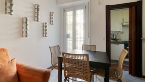 Een eetgedeelte met een tafel en stoelen, een bank, en een keuken die door een open deur zichtbaar is.