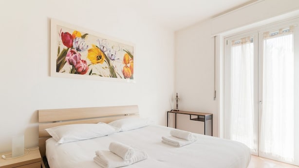 Een hotelkamer met een bed, nachtkastje, bureau en raam met gordijnen.