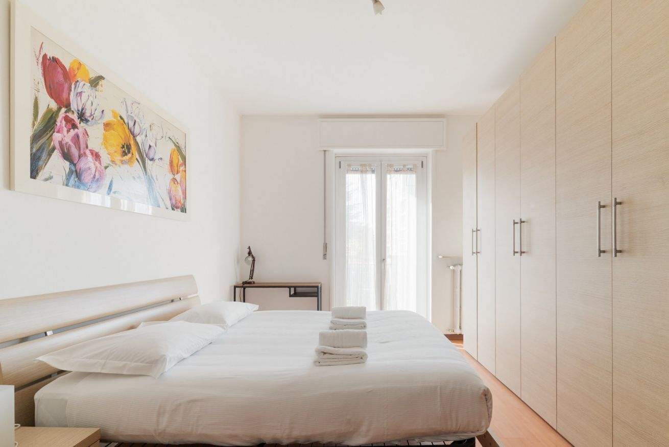 A bedroom with a bed, a nightstand, a desk, a wardrobe, and a painting on the wall.