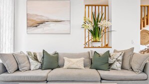 Un sofá de tonos neutros con varios cojines, una mesita de madera con un cuenco y una obra de arte enmarcada sobre el sofá.