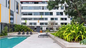 A modern building with a swimming pool, lounge chairs, and various plants. - Chic 1 Bed Inner-City Retreat with Pool and Views (Fortitude Valley)
