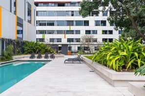 Un bâtiment moderne doté d’une piscine, de chaises longues et de diverses plantes.