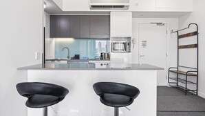 A modern kitchen with a central island, two black bar stools, and a built-in oven. - Chic 1 Bed Inner-City Retreat with Pool and Views (Fortitude Valley)