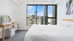 A hotel room with a large window, a bed, a desk, and a city view. - Chic 1 Bed Inner-City Retreat with Pool and Views (Fortitude Valley)