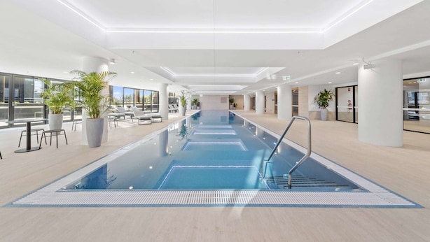 A modern indoor swimming pool with clear blue water, surrounded by lounge areas and large windows. - Phillip 2-Bed: Chic Interiors, Amazing Amenities (Phillip)