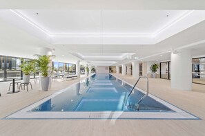 Una piscina interior moderna con agua cristalina, rodeada de zonas de descanso y amplias ventanas.