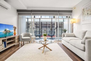 En moderne stue med et fladskærms-tv, en sofa, et sofabord og en balkon med stole og en plante.