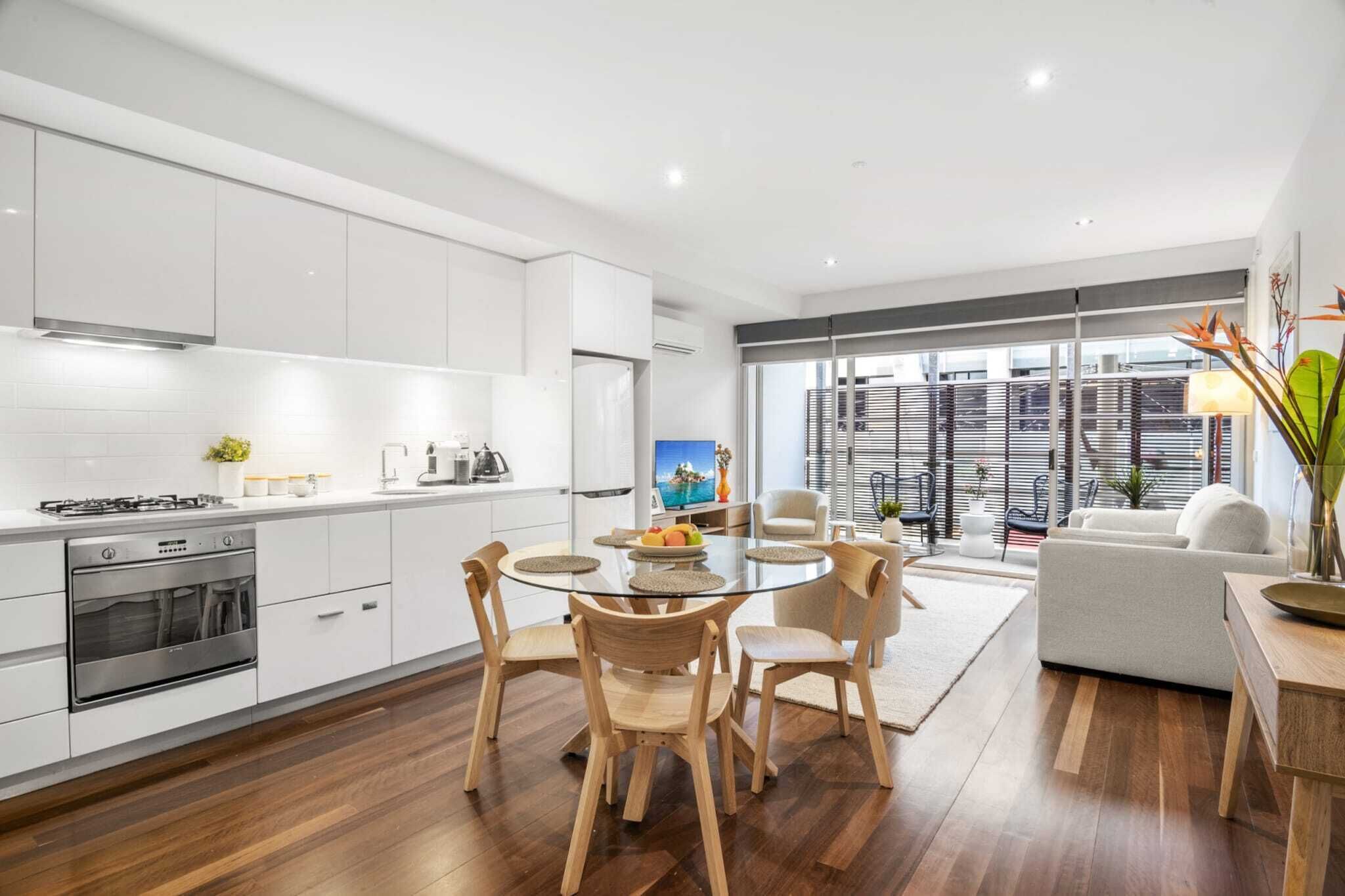 A modern kitchen with white cabinets, a dining table with chairs, and a living area with a sofa and a coffee table.