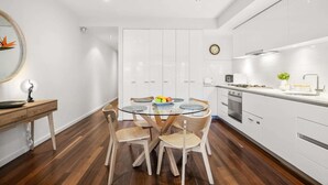 Een moderne keuken met witte kastjes, een ronde glazen tafel en houten stoelen.