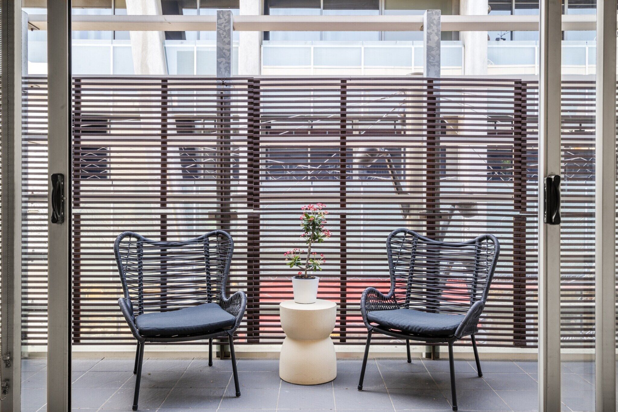 Ein Balkon mit zwei schwarzen Korbstühlen, einem kleinen runden Tisch und einem Blumentopf.
