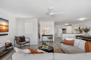 A modern living room with a sofa, armchair, coffee table, and a dining area with a table and chairs. - 3-Bed Haven with Balcony and BBQ, 5-Min to Beach (Coolum Beach)