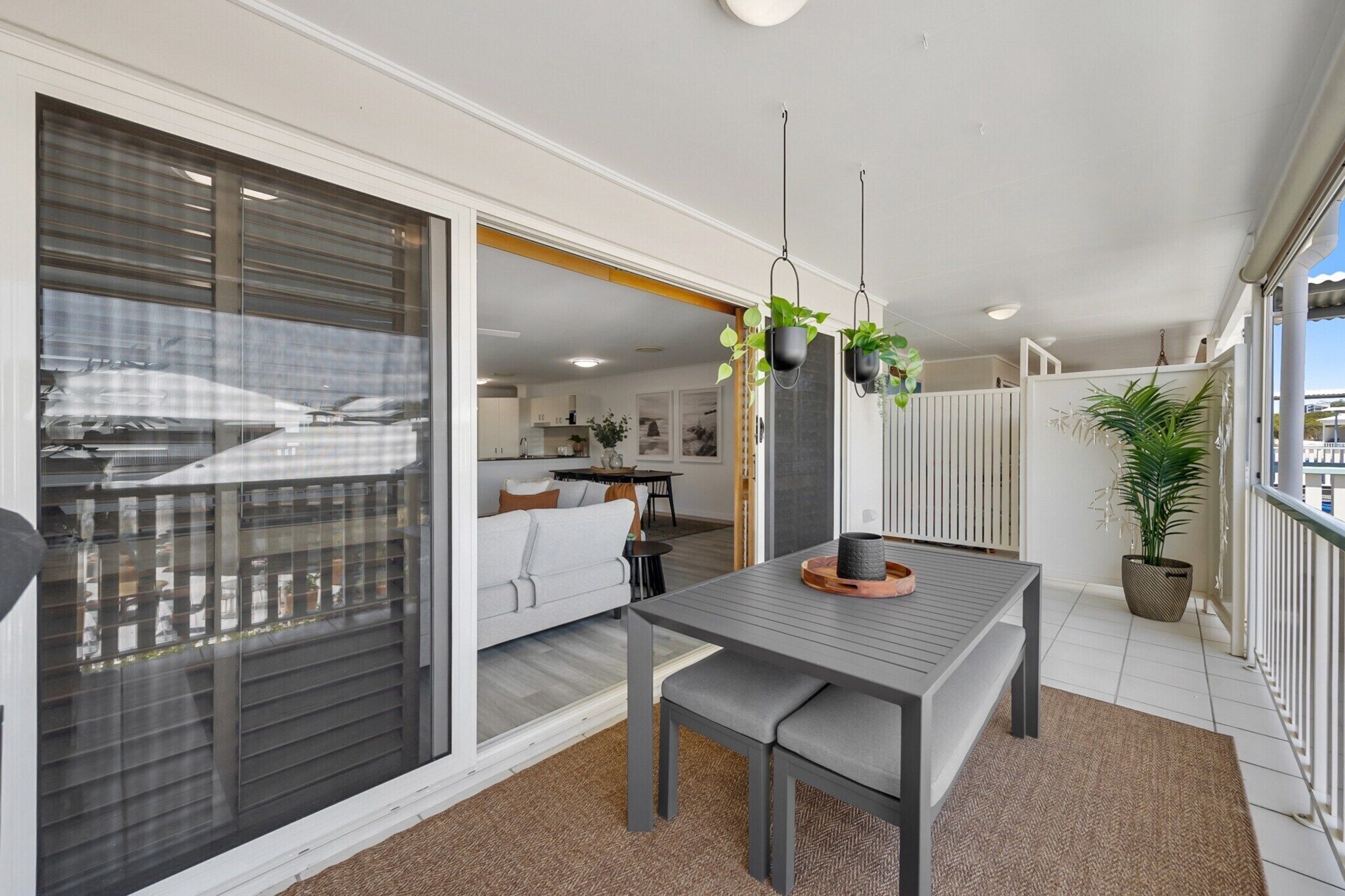 A modern living area with a sliding glass door leading to a balcony, a dining table with a bench, and potted plants.