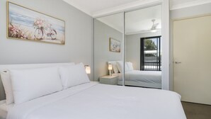 A hotel room with a large bed, a nightstand, a lamp, a mirror, and a painting on the wall.