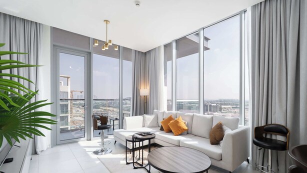 Ein modernes Wohnzimmer mit einem weißen Sofa, einem runden Couchtisch und Blick auf eine Stadtkulisse durch große Fenster.