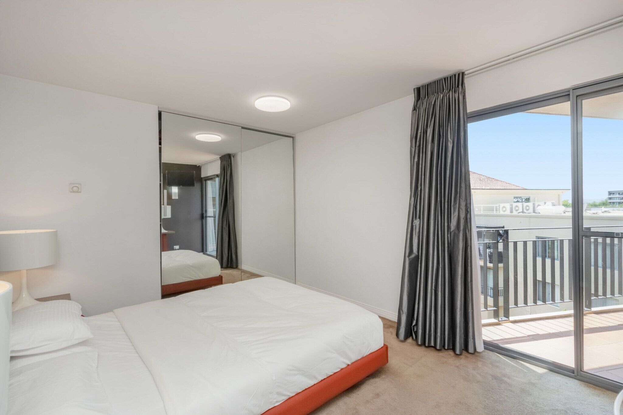 Une chambre d’hôtel avec un lit, un miroir, une fenêtre avec des rideaux et un balcon doté d’une balustrade.