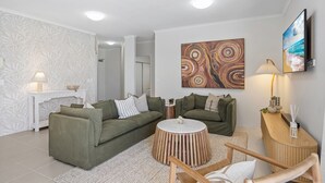 A modern living room with two green sofas, a round coffee table, a wooden side table, and a TV mounted on the wall.