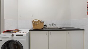 A compact laundry area with a washing machine, a sink, and a basket on the countertop.