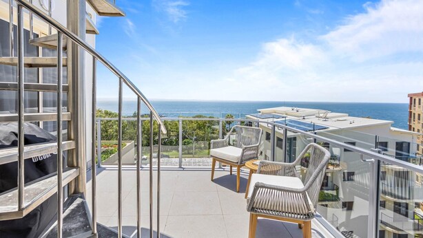 A balcony with a view of the sea, wicker chairs, and a grill.