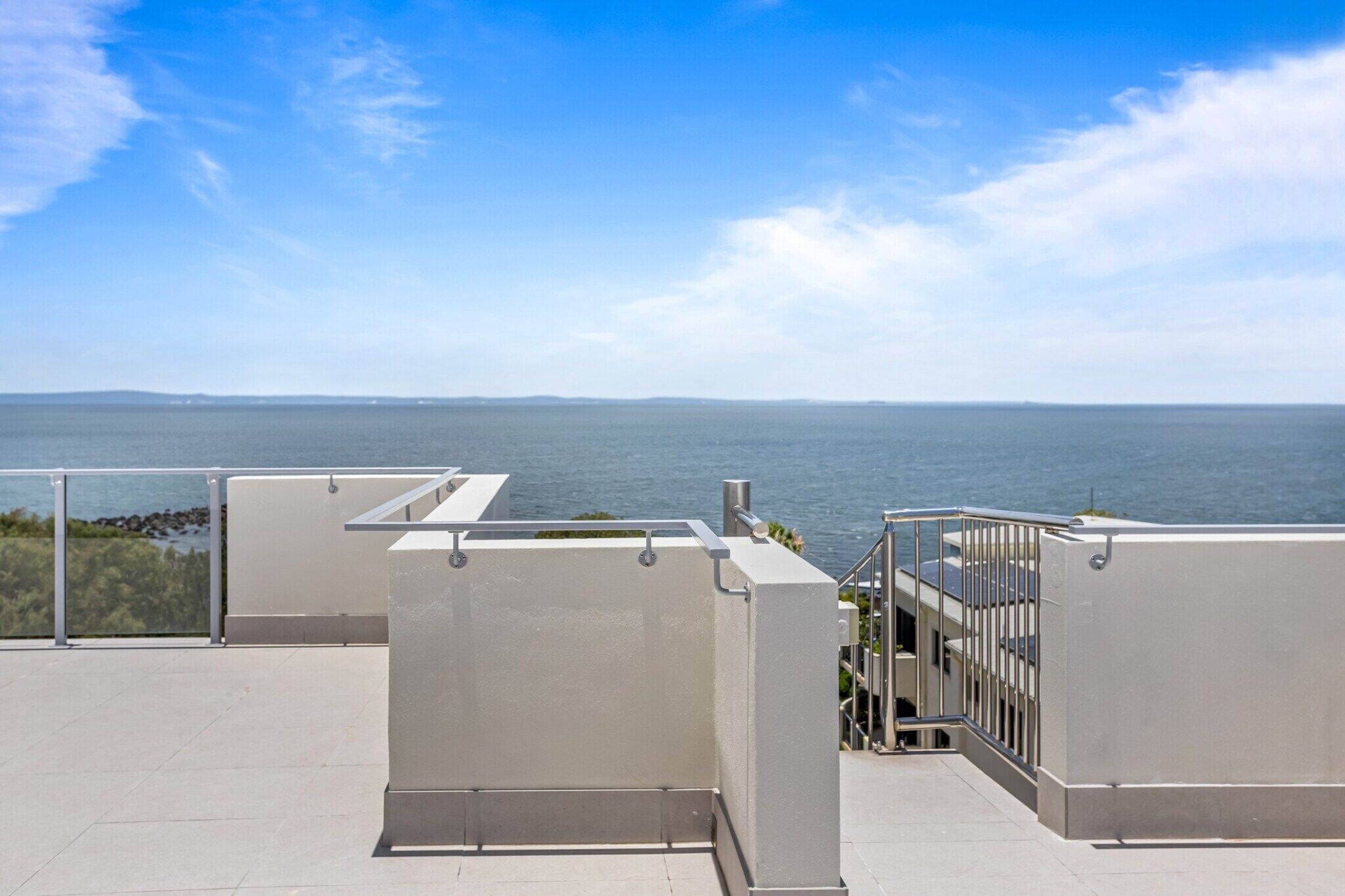En tagterrasse med udsigt over havet, præget af moderne arkitektur med metalgelændere og flisebelagt gulv.
