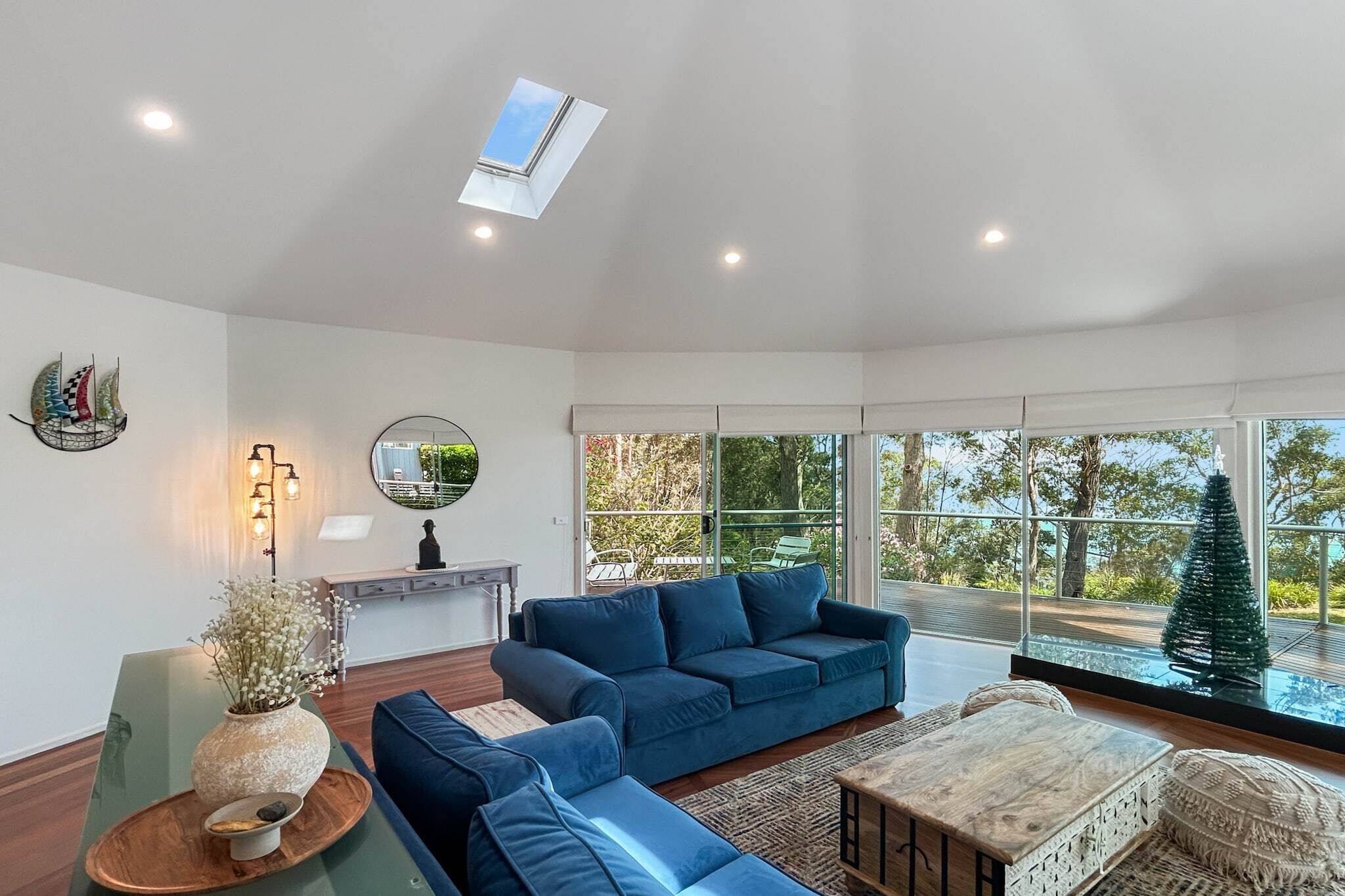 A modern living room with a blue sofa, a wooden coffee table, and a large window with a view of greenery.