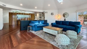 Uma sala ampla com dois sofás azuis, uma mesa de centro de madeira e um tapete estampado.