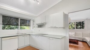 A modern kitchen with white cabinetry, a built-in dishwasher, and a window with blinds. - Riverside 3-Bed Townhouse with Spacious Deck & BBQ (Mossy Point)
