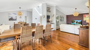A spacious living area with a wooden dining table and wicker chairs, a white sofa, and a TV. - Riverside 3-Bed Townhouse with Spacious Deck & BBQ (Mossy Point)