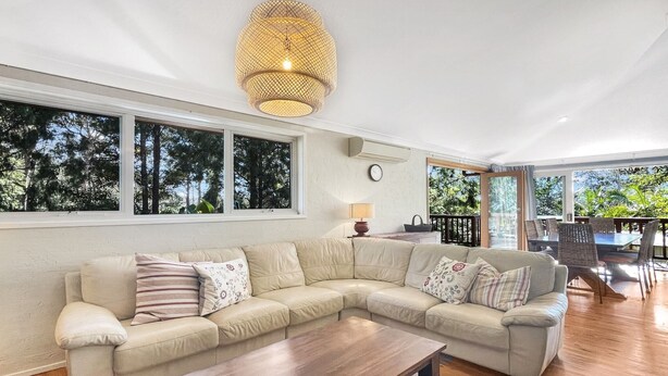 A spacious living room with a large beige sectional sofa, a wooden coffee table, and a hanging light fixture. Large windows provide a view of the outdoors. - Riverside 3-Bed Townhouse with Spacious Deck & BBQ (Mossy Point)