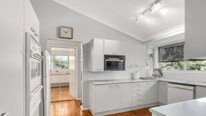 A modern kitchen with white cabinetry, a built-in microwave, and a window with blinds. - Riverside 3-Bed Townhouse with Spacious Deck & BBQ (Mossy Point)
