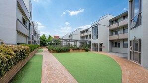 Ett modernt bostadskomplex med en central innergård, belagda gångvägar och en mängd olika växter och grönska.