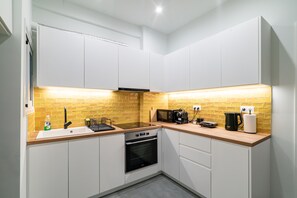 Een kleine keuken met witte kastjes, een houten aanrecht, een inbouwoven en een magnetron.