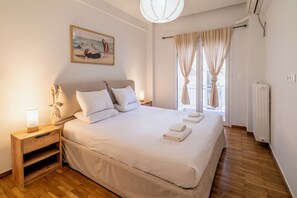 Een netjes opgemaakt bed met witte lakens en kussens, een bedlampje en een nachtkastje met lamp.
