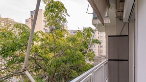 Ein Balkon mit weißer Brüstung, Fliesenboden und Blick auf Bäume und Gebäude.