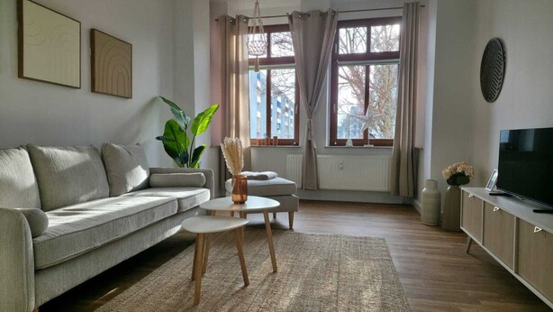 Un salon avec un canapé gris, une table basse, un téléviseur et une plante.