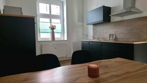Une cuisine moderne avec des meubles de couleur sombre, une table en bois et une fenêtre équipée de stores.