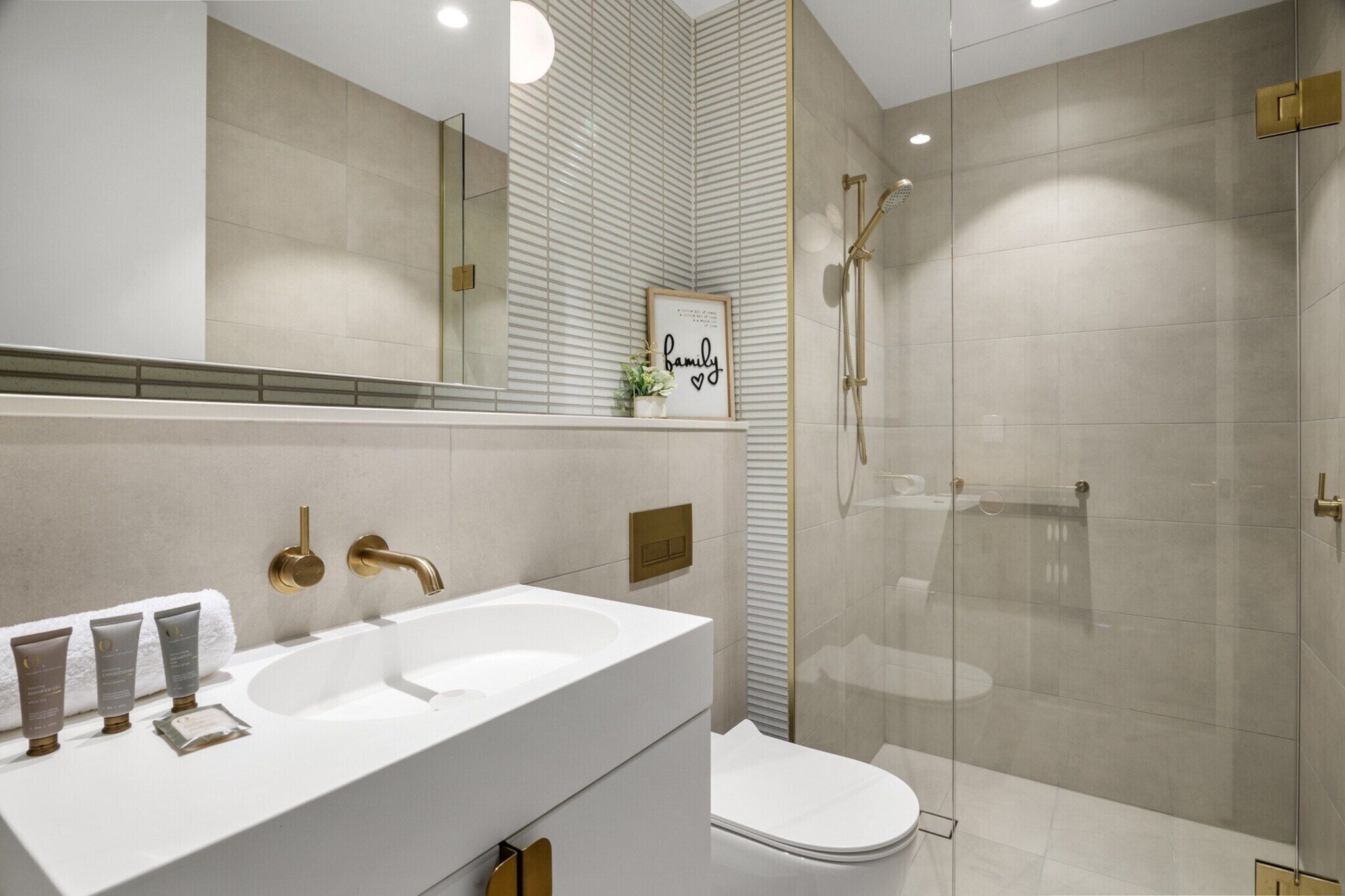 A modern bathroom with a white sink, gold fixtures, and a glass-enclosed shower.