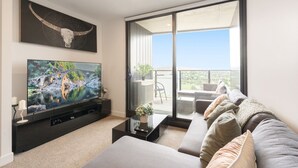 Ein modernes Wohnzimmer mit großem Flachbildfernseher, einer Couch, einem Couchtisch und einem Balkon mit Aussicht.