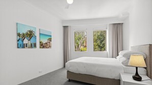 A hotel room with a bed, a nightstand, a lamp, and two windows with curtains. - Chic Urban Escape in Vibrant Camperdown (Camperdown)