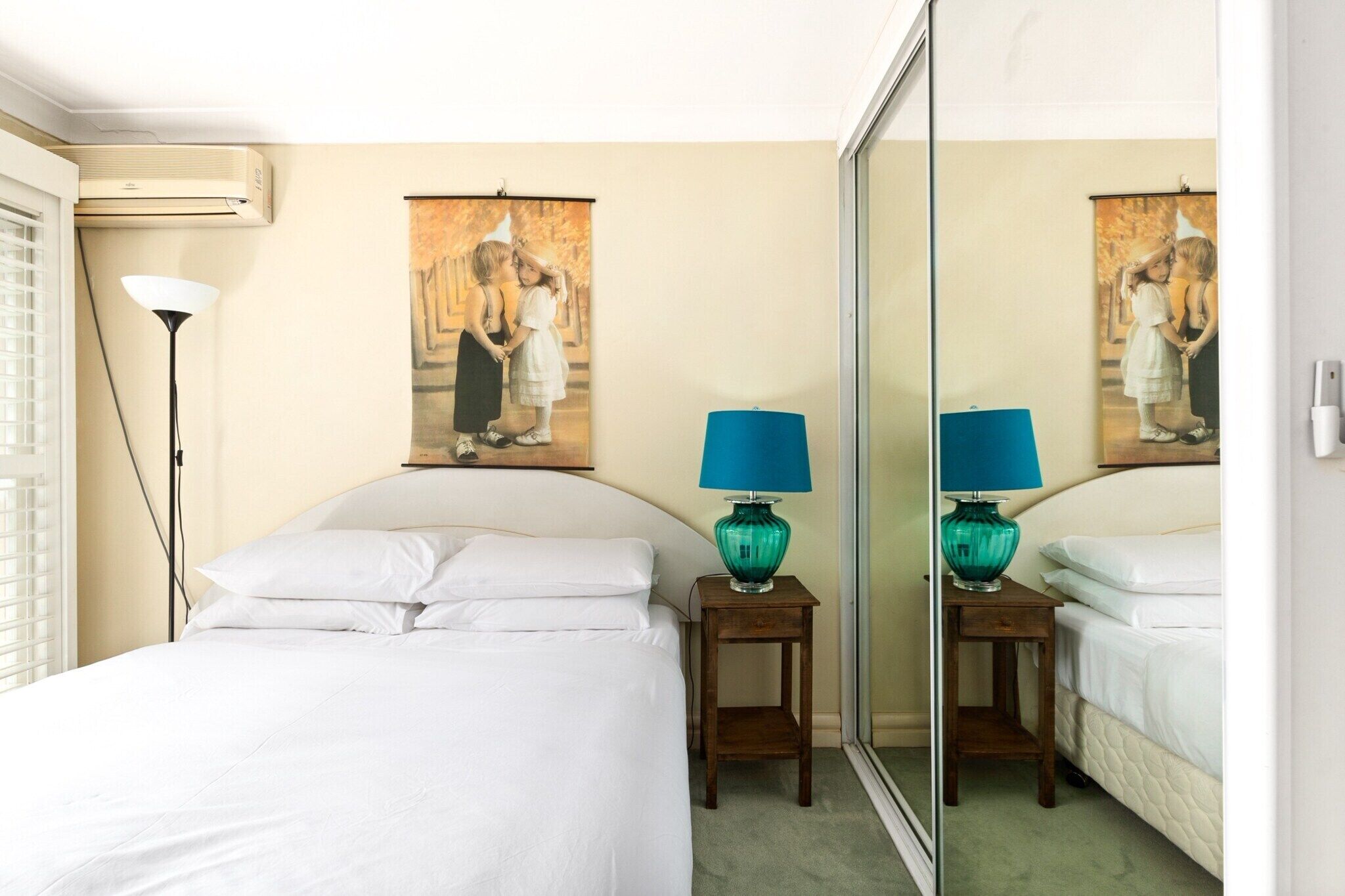 Une chambre d’hôtel avec un lit, deux tables de chevet, une lampe, un miroir et un tableau au mur.