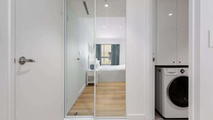 Ein modernes Hotelzimmer mit einer Glastür, die auf einen Balkon führt, einer Waschmaschine und einem Bett mit blauer Vorhang.