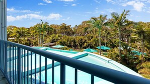 A pool area with a blue railing, surrounded by palm trees and a clear blue sky. - Resort-Style Stay with Balcony & Garage Parking (Torquay)