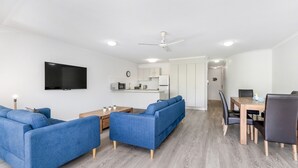 A modern living room with a sofa set, a dining table with chairs, and a kitchen area in the background. - Resort-Style Stay with Balcony & Garage Parking (Torquay)