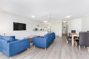 A modern living room with a sofa set, a dining table with chairs, and a kitchen area in the background. - Resort-Style Stay with Balcony & Garage Parking (Torquay)