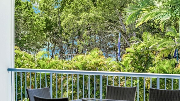 A balcony with wicker furniture and a view of dense tropical foliage. - Resort-Style Stay with Balcony & Garage Parking (Torquay)