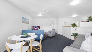 Ein modernes Wohnzimmer mit einem blauen Sofa, einem grauen Sessel und einem weißen Esstisch mit Stühlen.