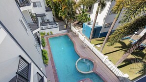 Ein Pool auf dem Dach mit einer runden Whirlwanne, umgeben von einem weißen Zaun und Palmen.